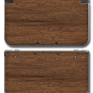 Puede incluir: Una consola de juegos portátil con un diseño de veta de madera marrón en la carcasa exterior. El dispositivo se muestra desde los ángulos superior e inferior, exhibiendo el acabado texturizado marrón oscuro, bisagras y tornillos visibles.