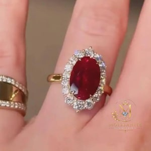 Peut inclure: Une bague en or avec une grande pierre rouge taille ovale entourée d'un halo de petites pierres blanches, et une seconde bague en or avec une large section centrale polie bordée de deux rangées de petites pierres blanches.