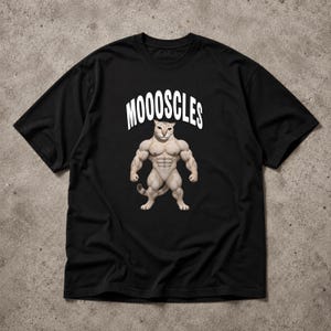 Może przedstawiać: Czarny t-shirt z krótkim rękawem z grafiką umięśnionego kota stojącego na tylnych łapach. Nad kotem znajduje się napis MOOOSCLES wykonany białymi wielkimi literami. Kot ma beżową sierść i bardzo wyraźnie zarysowane, przesadne mięśnie.