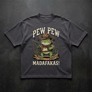 May include: A charcoal gray t-shirt featuring a graphic of a green frog dressed as a cowboy, wearing a brown hat and vest, holding two revolvers. The text PEW PEW MADAFAKAS! is printed in white above and below the frog, with a lasso and cacti.