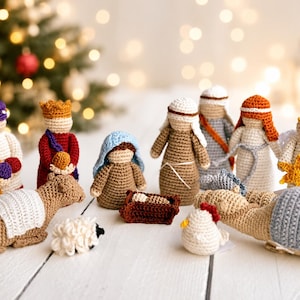May include: A crochet nativity set featuring various figures including a central infant in a manger, a blue-hooded figure, three standing figures in robes, an angel with a yellow star, a sheep, a chicken, and two camels with textured blankets.