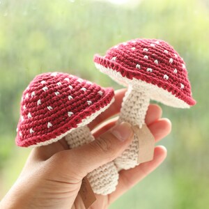 May include: Two crocheted mushroom toys, one red with white dots and one white, held in a hand.