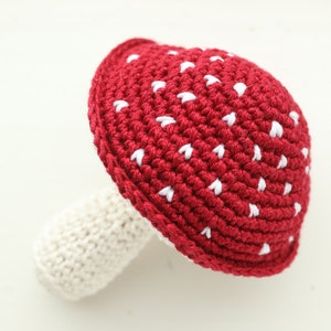 May include: A crocheted red mushroom with white spots. The mushroom has a white stem.