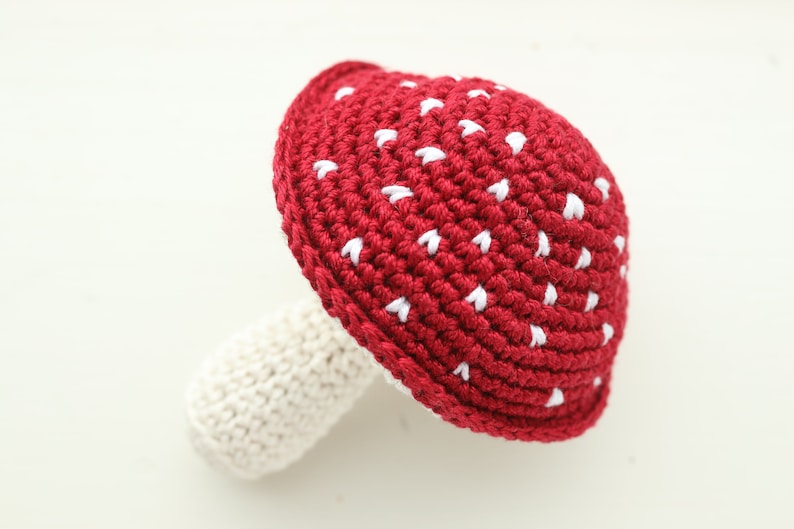 May include: A crocheted red mushroom with white spots. The mushroom has a white stem.