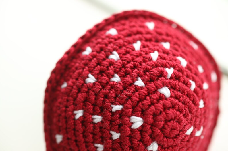 May include: Close-up of a red crocheted hat with white heart-shaped details.