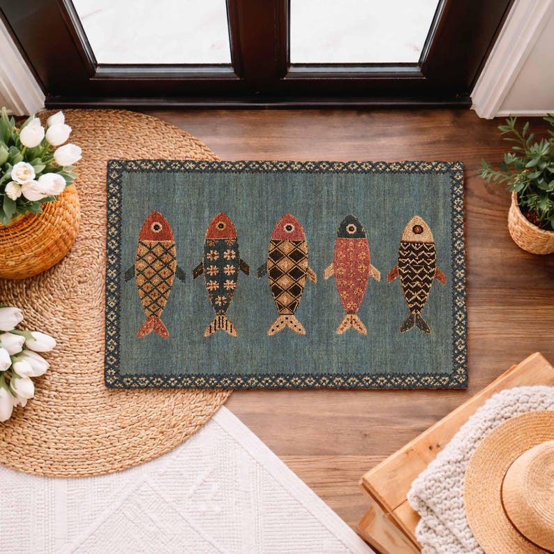 May include: A rectangular doormat with a blue-grey background featuring five stylized fish arranged in a horizontal row. Each fish displays a unique geometric pattern in shades of red, black, and tan, enclosed by a dark decorative border.