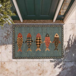 May include: A rectangular doormat with a teal background and a dark border featuring a repeating geometric pattern. Five stylized fish are arranged horizontally across the center, each decorated with unique, intricate patterns in shades of red, orange, and black.