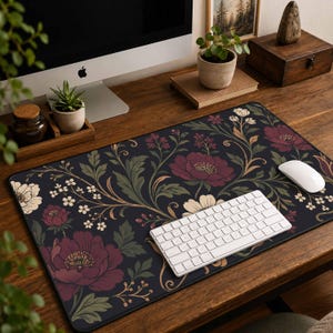 May include: A rectangular desk mat featuring a dark navy blue background with a repeating floral pattern of large burgundy peonies, cream-colored blossoms, and muted green foliage. A white wireless keyboard and a white computer mouse sit on top.
