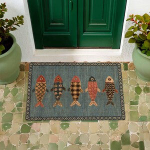May include: A rectangular doormat with a blue-grey background featuring five stylized fish arranged in a horizontal row. Each fish displays a unique geometric pattern in shades of red, orange, black, and cream, framed by a dark decorative border.