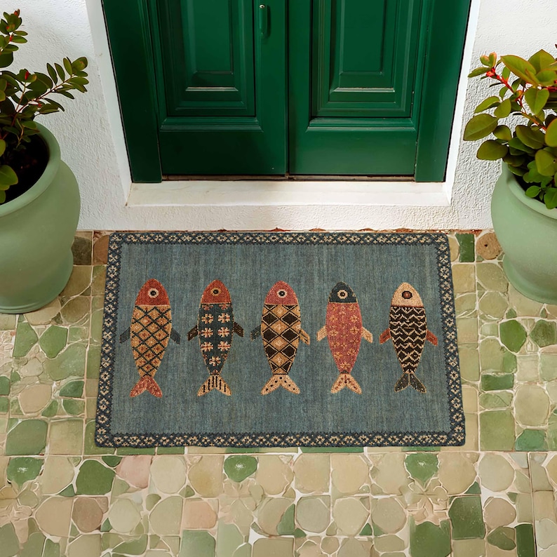 May include: A rectangular doormat with a blue-grey background featuring five stylized fish arranged in a horizontal row. Each fish displays a unique geometric pattern in shades of red, orange, black, and cream, framed by a dark decorative border.