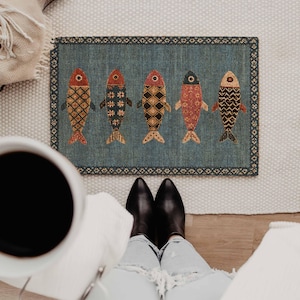 May include: A rectangular doormat with a blue background featuring five stylized fish arranged in a row. Each fish displays a unique geometric pattern in shades of red, orange, black, and cream. The mat is framed by a decorative border.