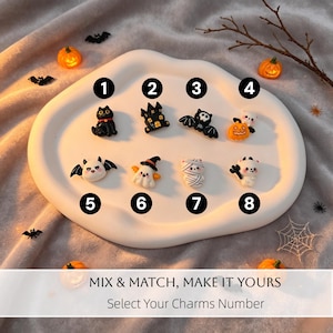 Puede incluir: Una colección de ocho pequeños dijes con temática de Halloween numerados del uno al ocho, que incluyen un gato negro, una casa embrujada, un murciélago, una calabaza, un fantasma y una momia. El texto MIX & MATCH, MAKE IT YOURS es visible.