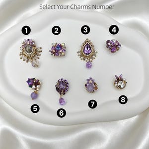 Puede incluir: Ocho dijes decorativos numerados del 1 al 8, con cristales morados y lavanda, perlas de imitación y detalles en metal dorado. El texto MIX & MATCH, MAKE IT YOURS y Select Your Charms Number aparece sobre la colección de piezas de joyería.