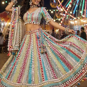Pode incluir: Um conjunto lehenga choli multicolorido com listras verticais em tons de azul-petróleo, amarelo e vermelho. A peça é ricamente adornada com pequenos espelhos, bordados complexos e conchas de búzios brancas na bainha e nas mangas.