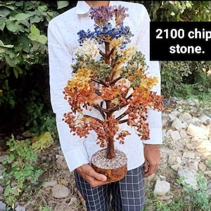 Puede incluir: Una escultura de árbol decorativa con 2100 astillas de piedra en un degradado de colores que incluye morado, azul, blanco, verde, amarillo, naranja y rojo. El árbol tiene un tronco y ramas marrones, sobre una base circular con acabado de piedra.
