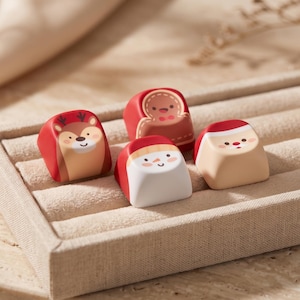 Puede incluir: Un conjunto de cuatro teclas personalizadas para teclado mecánico con ilustraciones de temática navideña. Los diseños incluyen un reno marrón, un hombre de jengibre beige, un muñeco de nieve blanco y una cara de Papá Noel sobre fondo rojo.