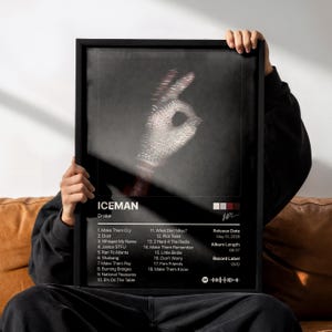 Puede incluir: Un póster negro enmarcado que muestra una mano brillante incrustada de diamantes haciendo un gesto de ok. El texto dice ICEMAN de Drake, con una lista de 18 canciones, fecha de lanzamiento 15 de mayo de 2026, duración 68:37, sello OVO y una firma.