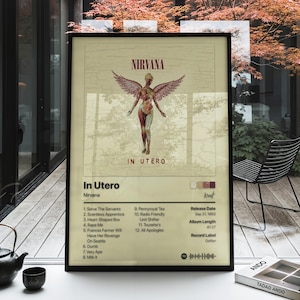 May include: A framed poster of the Nirvana In Utero album cover featuring a winged figure, tracklist, release date of September 21, 1993, album length of 41:27, record label Geffen, and a Spotify code on a cream-colored background with black text.