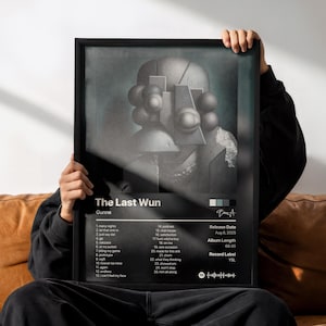 Puede incluir: Un póster enmarcado en blanco y negro del álbum The Last Wun de Gunna. La obra muestra una figura abstracta estilizada con elementos esféricos. Debajo de la imagen, la lista de canciones, la fecha de lanzamiento del 8 de agosto de 2025 y el sello YSL están impresos en texto blanco sobre un fondo oscuro.