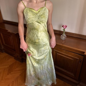 Può includere: Un abito lungo in raso verde lime con scollo a cuore e tessuto arricciato e plissettato sul corpetto. L'abito presenta sottili spalline e un delicato motivo floreale giallo che si ripete su tutto il tessuto fino all'orlo inferiore.