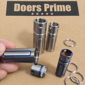 May include: Three cylindrical metal pill containers with blue accents and threaded caps. Each container features a top section with circular holes and a main body with vertical grooves. Three metal key rings are included in the set.