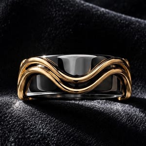 Könnte beinhalten: Ein breiter Ring mit einem polierten schwarzen Mittelteil, der durch zwei ineinander verschlungene, wellenförmige goldfarbene Metalldrähte kontrastiert wird, die die Außenfläche umschließen und ein geschichtetes, dreidimensionales Aussehen mit glatter Oberfläche erzeugen.