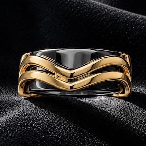 Puede incluir: Un anillo con una banda de cerámica negra pulida acentuada por dos bandas metálicas doradas onduladas y superpuestas que envuelven el centro. El diseño muestra un contraste entre el material oscuro y liso y los elementos metálicos curvos y brillantes.