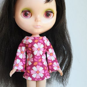 Könnte beinhalten: Eine Puppe mit langen schwarzen Haaren, die ein rosa-weißes Blumenkleid mit Glockenärmeln trägt.