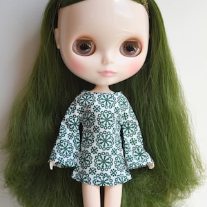May include: A doll with long green hair wearing a white dress with a green snowflake pattern.