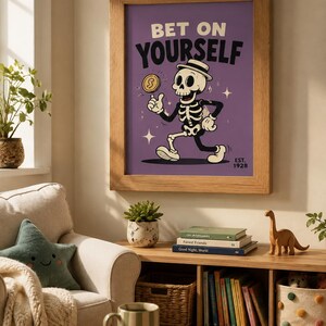 May include: A framed wall art print featuring a cartoon skeleton wearing a hat, holding a gold coin, and walking against a purple background. The text reads BET ON YOURSELF and EST. 1928. The print is enclosed in a light brown wooden frame.