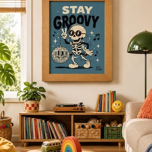 May include: A framed wall art print featuring a cartoon skeleton wearing sunglasses and making a peace sign. The skeleton stands next to a disco ball on a blue background with the text STAY GROOVY and EST. 1928. Musical notes and stars surround the figure.