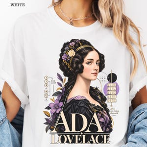 May include: A white t-shirt featuring a graphic of Ada Lovelace with dark hair adorned with purple and yellow flowers. The design includes a flow chart, a punch card illustration, and the text "ADA LOVELACE" and "Ideas can change the world."