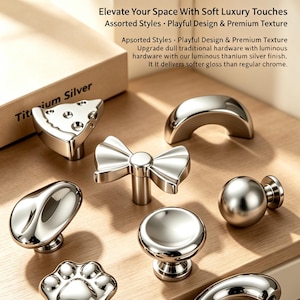 May include: A collection of titanium silver cabinet hardware in various shapes including a bow, a paw print, a sphere, a crescent, and a cheese wedge. The text Titanium Silver Cabinet Hardware is visible on a box in the background of the display.