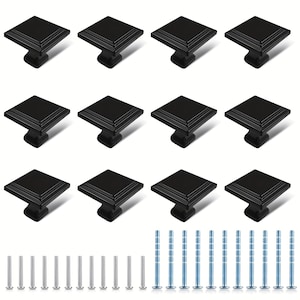 May include: A set of twelve square cabinet knobs in a matte black finish, each featuring a stepped edge design. The collection includes twelve short silver-toned mounting screws and twelve long silver-toned breakaway screws for installation.