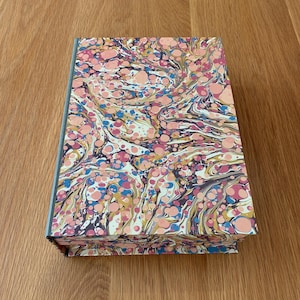 May include: A rectangular box featuring a marbled pattern on its exterior surface. The design consists of swirling, organic shapes in shades of pink, dark blue, yellow, and white, creating a dense, multi-coloured abstract effect across the lid.
