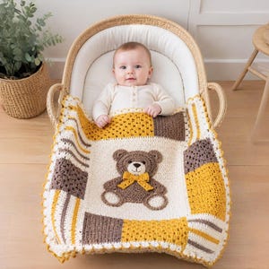May include: A handmade crochet baby blanket featuring a central square with a brown teddy bear appliqué wearing a yellow bow. The blanket is composed of alternating cream, mustard yellow, and brown squares with textured stitching and a scalloped edge.