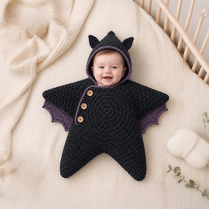 May include: A black crocheted star-shaped baby bunting with a hood featuring small pointed ears. The garment has three light brown wooden buttons along the side, purple trim along the hood and edges, and purple wing-like accents on the sides.