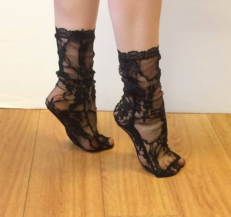 May include: A pair of black lace socks with a delicate floral pattern. The socks are sheer and have a ruffled top.