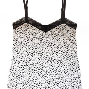 May include: A white tank top with black polka dots and black lace trim.