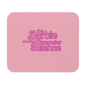 May include: A rectangular pink mouse pad featuring the dark pink text "this Barbie studies Computer Science" centered on the surface. The design uses a stylized, rounded font with the word Barbie appearing in a larger, prominent typeface.