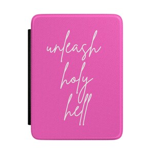 Peut inclure: Une housse de liseuse rectangulaire rose vif avec une surface texturée. Le devant présente le texte cursif blanc "unleash holy hell" centré verticalement. La housse a des coins arrondis et une tranche noire visible sur le côté gauche.