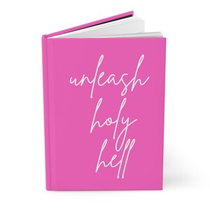 Peut inclure: Un livre à couverture rigide rose vif avec le texte en cursive blanche sur la couverture avant qui indique unleash holy hell. Le livre est légèrement ouvert, révélant des pages blanches sur le bord supérieur. Fond rose uni et lettrage blanc.