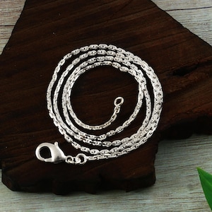 Può includere: Una collana a catena in metallo color argento composta da una serie di maglie ovali interconnesse. La collana è rifinita con una chiusura a moschettone lucida a un'estremità e un piccolo anello circolare all'altra estremità.