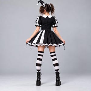Puede incluir: Un vestido blanco y negro con mangas cortas abullonadas, cuello redondo y falda acampanada con rayas verticales. El conjunto incluye un gorro de buf&oacute;n a juego con estampado de cuadros y calcetines altos a rayas blancas y negras.