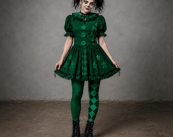 Puede incluir: Un disfraz de bufón verde oscuro que incluye un vestido de manga corta con cuello de volantes, tres botones grandes y una falda decorada con patrones de estrellas y rombos. El conjunto incluye un gorro de bufón a juego y leggings desiguales.