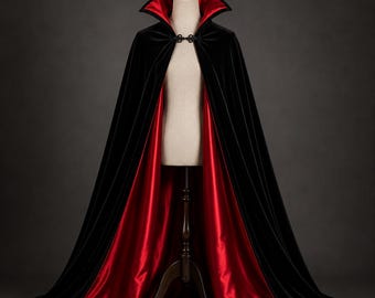 Puede incluir: Una capa de terciopelo larga hasta el suelo con un exterior negro profundo y un forro de satén rojo vibrante. La prenda incluye un cuello alto estructurado y un cierre decorativo de metal negro en el escote, diseñada para caer desde los hombros.