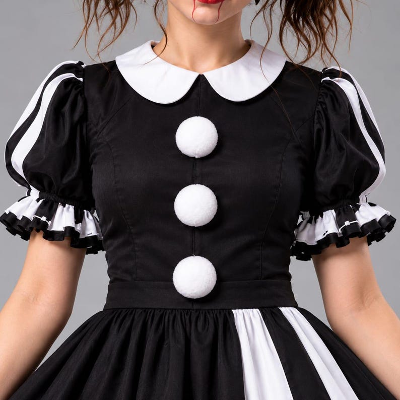 Puede incluir: Un vestido en blanco y negro con cuello redondo blanco, tres grandes botones de pomp&oacute;n blancos en el centro y mangas cortas abullonadas con pu&ntilde;os de volantes blancos y negros. El corpi&ntilde;o es negro liso y la falda tiene rayas verticales.