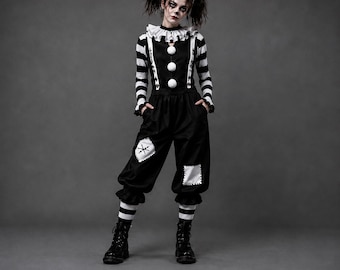 Puede incluir: Un disfraz de payaso en blanco y negro que incluye una camiseta de rayas de manga larga con cuello de volantes, tres pompones blancos y pantalones negros con parches blancos. El conjunto incluye un gorro de bufón a juego y botas negras.