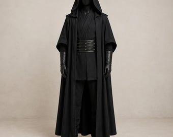 Puede incluir: Una capa negra con capucha de cuerpo entero sobre una túnica y pantalones negros a juego. El conjunto incluye un cinturón ancho negro estilo cuero con tachuelas plateadas y guantes negros largos. Se exhibe sobre un maniquí.