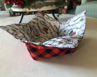 May include: A red and black plaid fabric bowl with a white fabric lining. The lining has a Christmas-themed print with holly leaves, a red truck, and the text "Over the River and Through the Woods to Grandmother's House We Go".